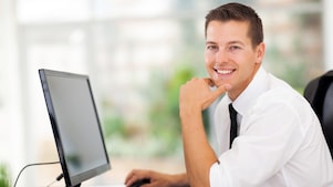 hombre rubio y sonriente, con ropa social, sentado frente a su ordenador.